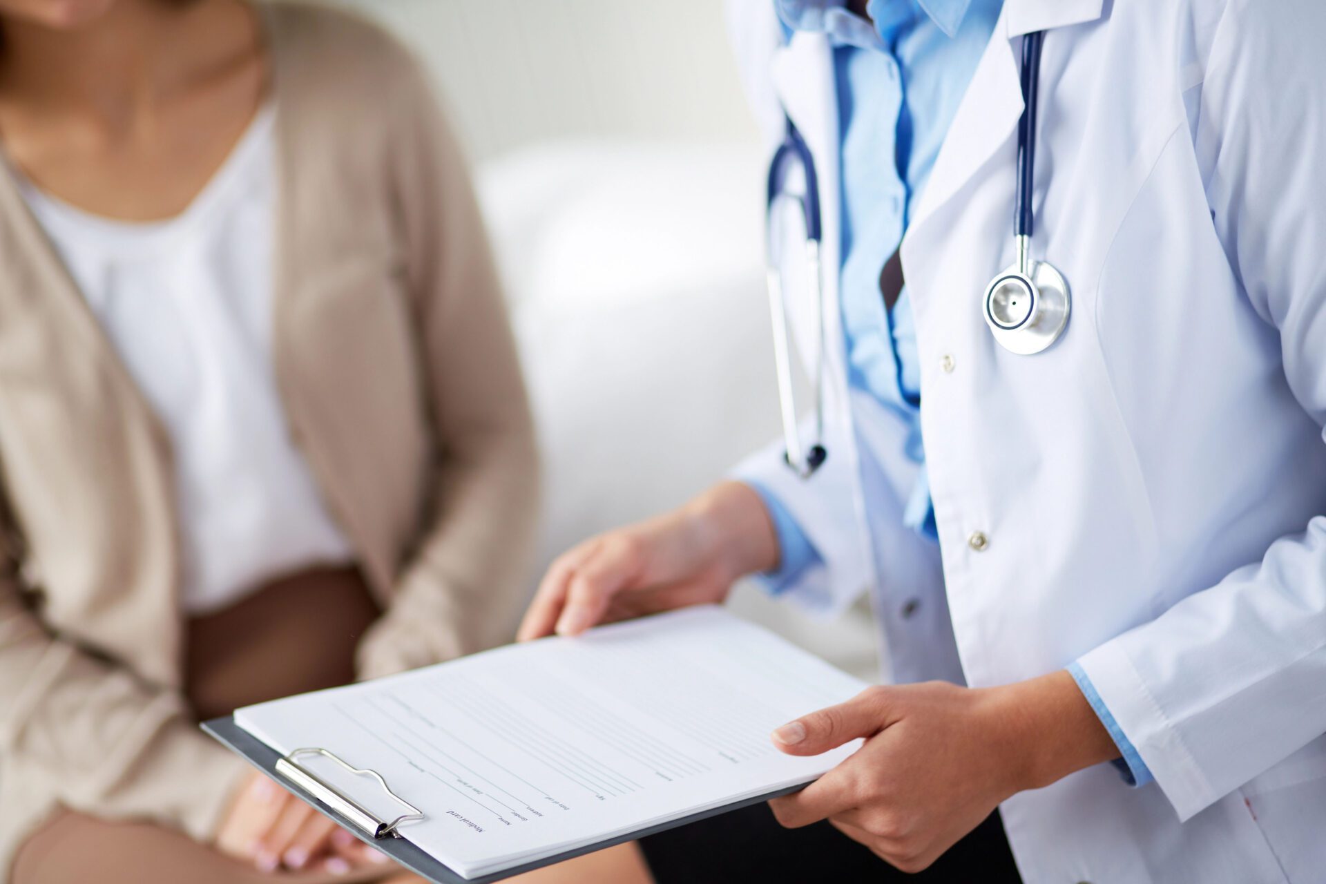 A doctor holding a clipboard with a patient in the background